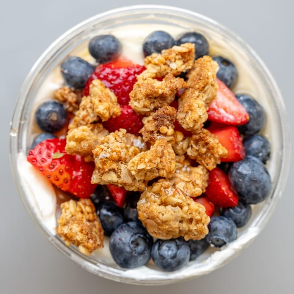 Overhead view of a healthy yogurt parfait with strawberries, blueberries, and granola in a clear cup.