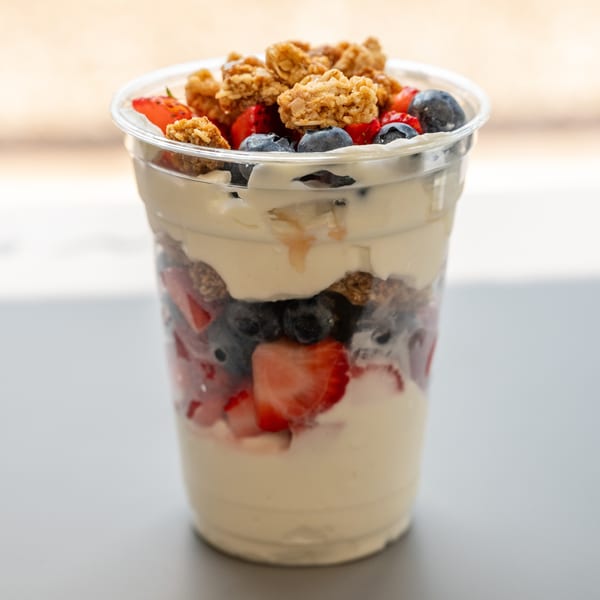 A healthy Blend Riverwalk parfait with layers of yogurt, blueberries, strawberries, and granola in a clear cup.