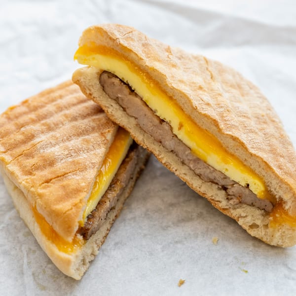 A healthy breakfast sandwich with egg, cheese, and sausage on toasted bread, cut in half.