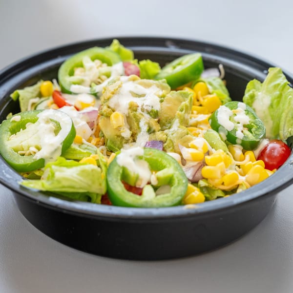 A healthy salad from Blend Riverwalk with lettuce, corn, tomatoes, avocado, and jalapeños, drizzled with dressing.
