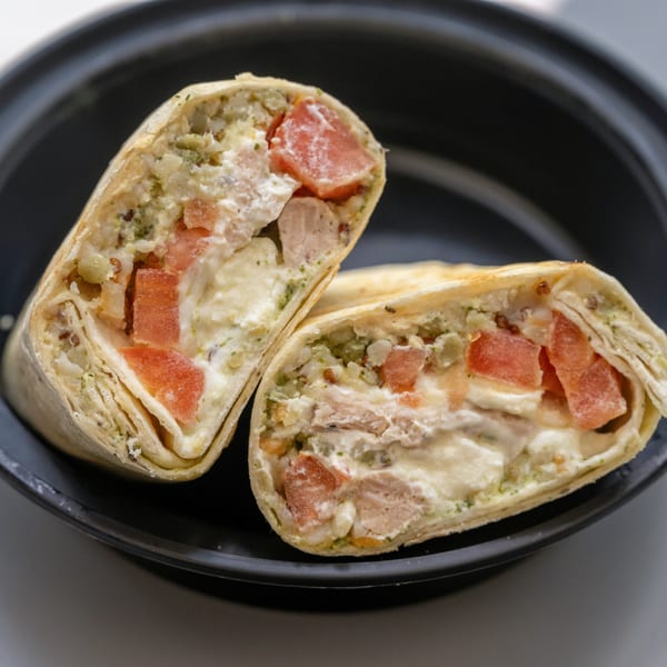 Two halves of a healthy wrap filled with chicken, tomatoes, and creamy sauce on a black plate.