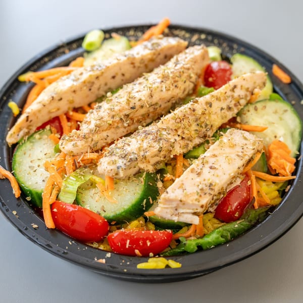 Blend Riverwalk's healthy chicken salad with cucumbers, carrots, and tomatoes in a black bowl.